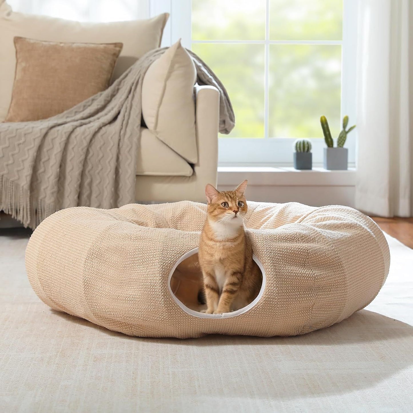 Beige donut cat play tunnel bed with round entrance opening and textured plush cover.