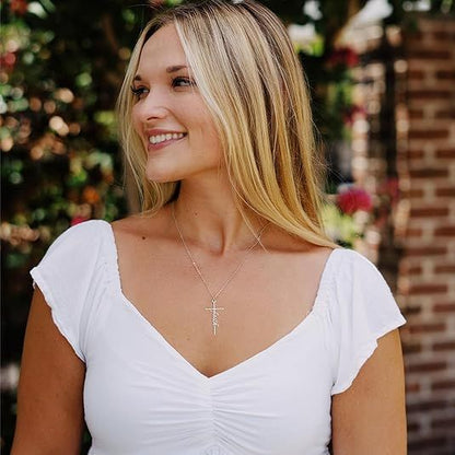 Woman wearing a silver cross pendant necklace with a small word charm.