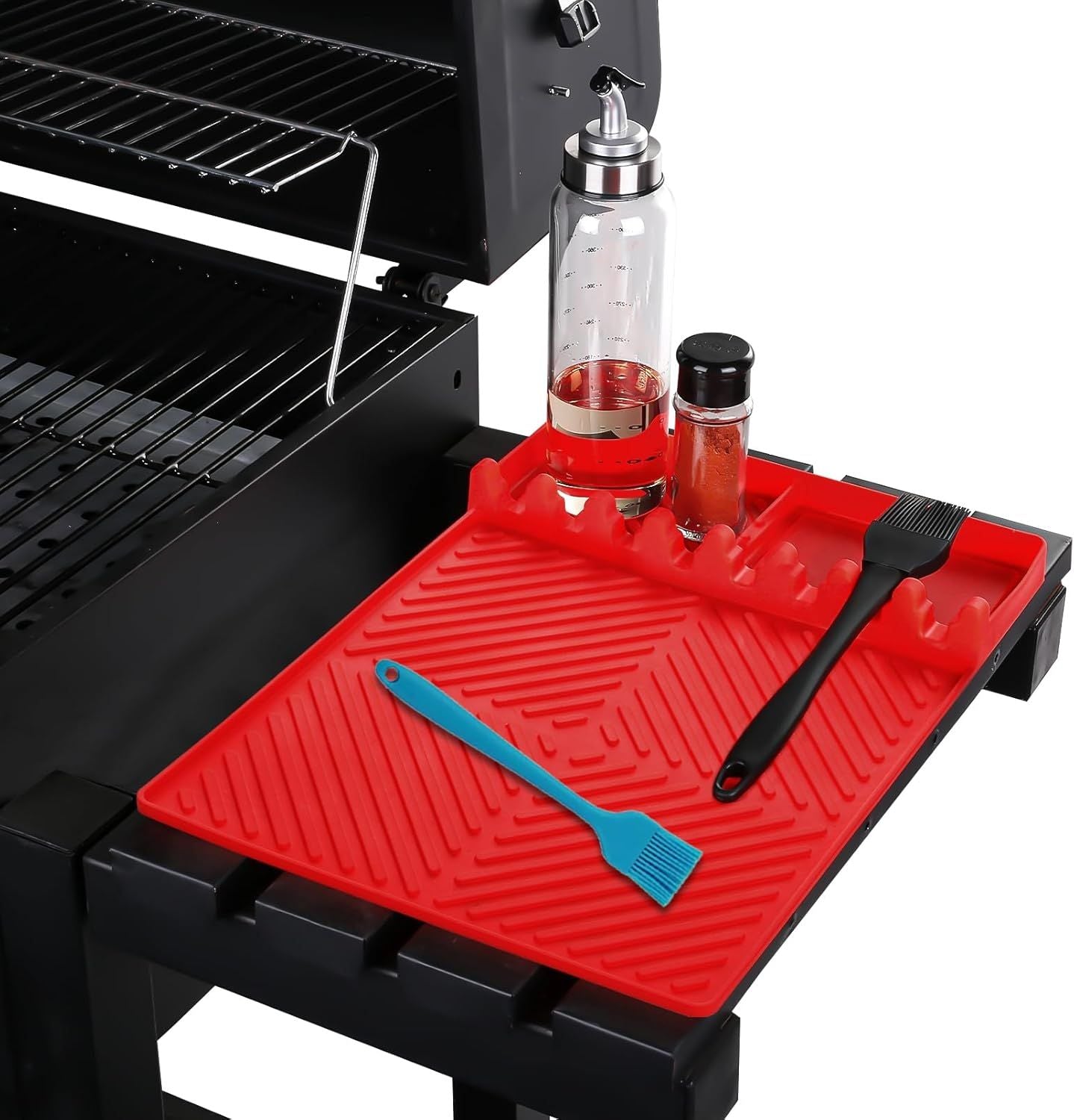 Red silicone tools mat on grill with central drip tray and slots for spatulas.