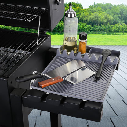 Gray silicone tools mat with ribbed drip pad and utensil slots beside grill