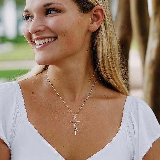 Close-up of a silver cross pendant necklace with a word charm on a delicate chain.