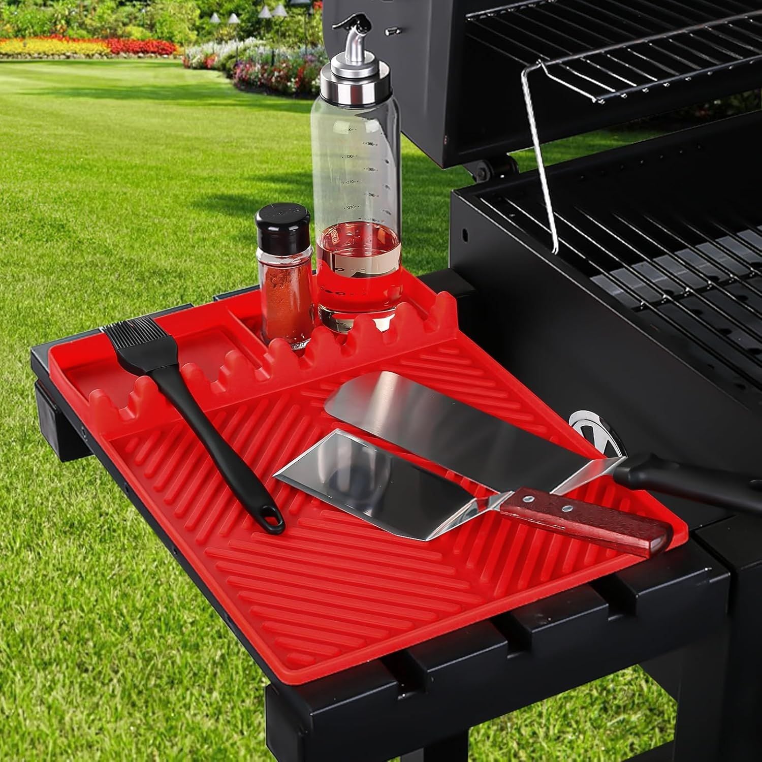 Red silicone tools mat on outdoor grill with central drip tray and utensil slots.